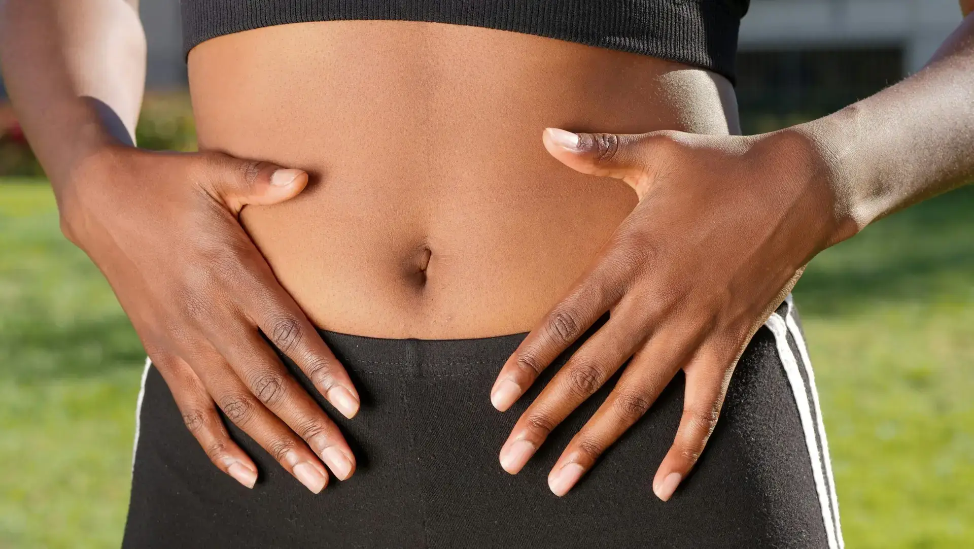Close-up of a person placing hands on stomach outdoors, emphasizing wellness, skin health, and outdoor exercise.