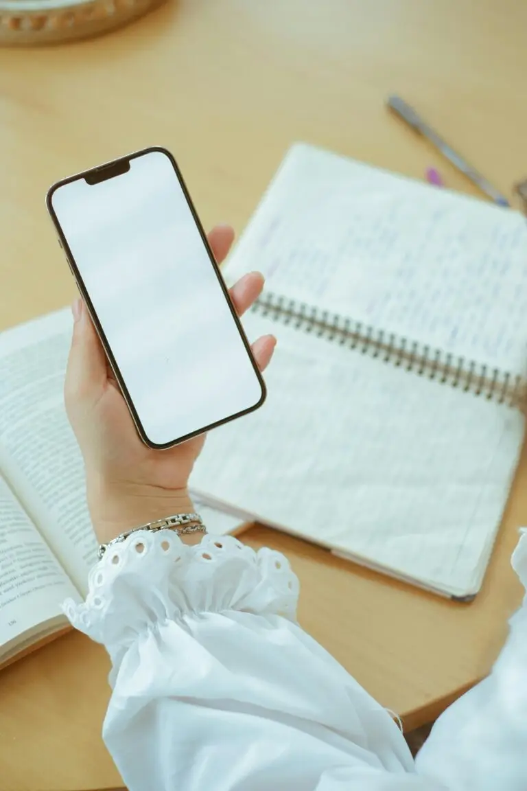 Close-up of a woman's hand holding a blank smartphone over open notebooks, ideal for mockup designs.